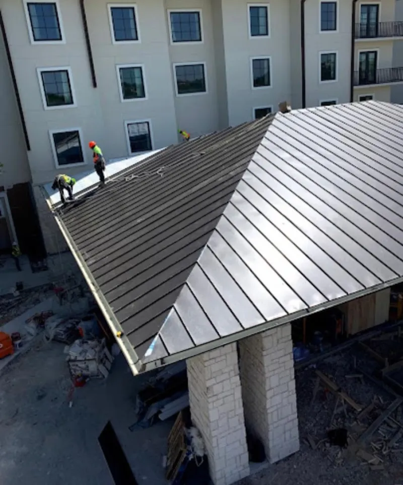 Crew installing standing seam metal roof panels on a commercial project in Clay